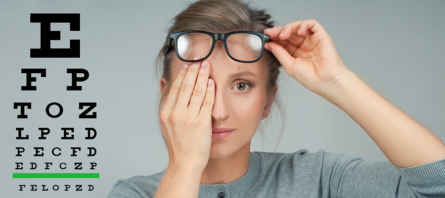 Woman with hand over eye next to an eye chart.